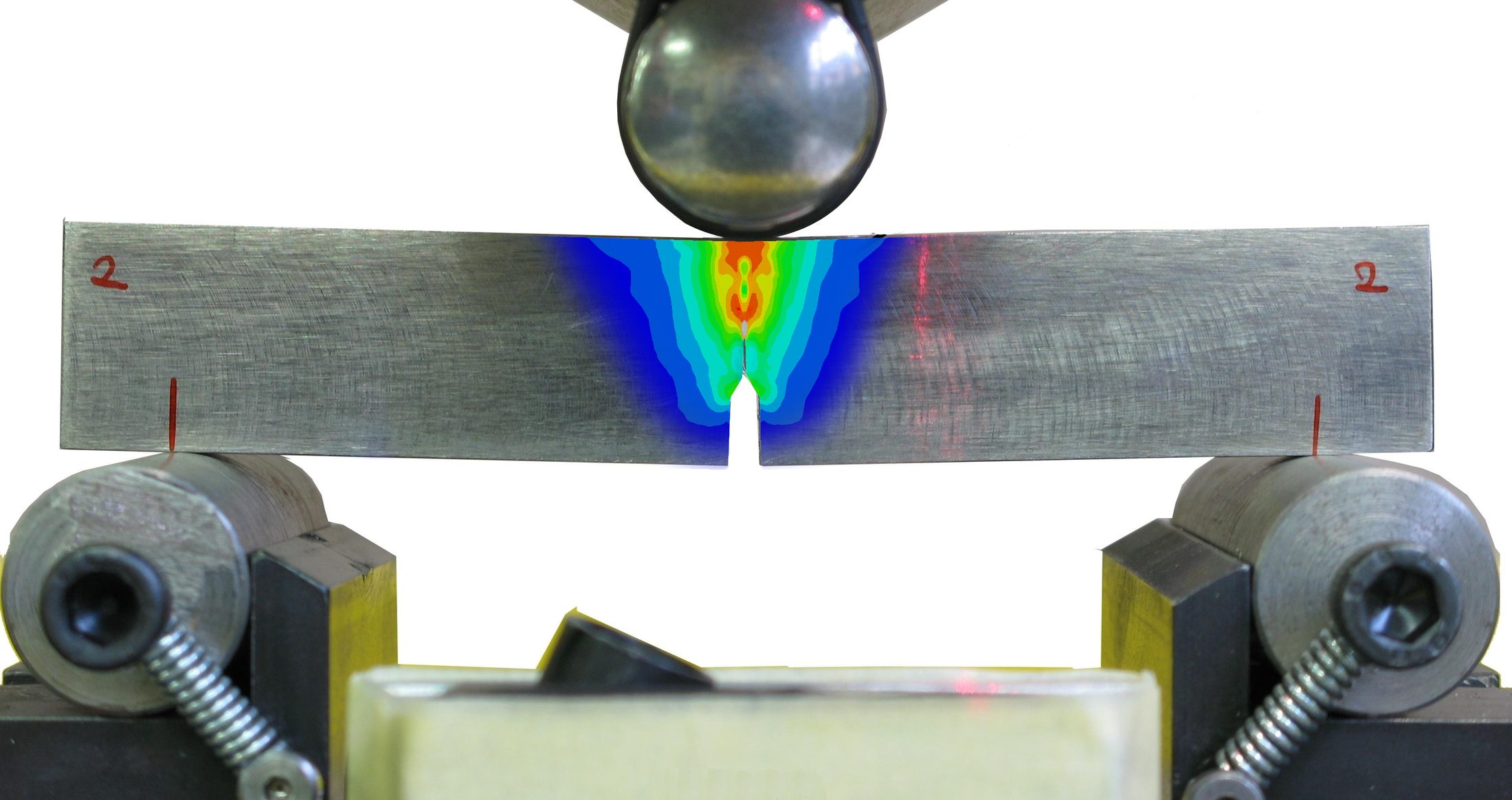Three-point bend test on a notched metallic specimen, with a digital image correlation strain field overlaid at the notch